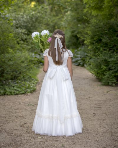 Girl walking through a park in Madrid on the day of her communion in a white dress surrounded by trees and nature