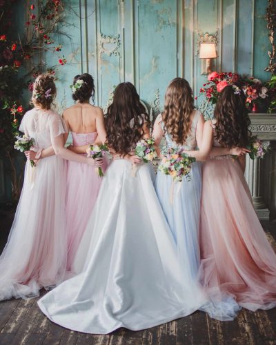 Bride and bridesmaids. Beautiful young women in dresses and with bouquets of fresh flowers. Back view