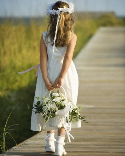 Rear view of a flower girl walking on a boardwalk holding a flower basket behind her back. Vertical shot.